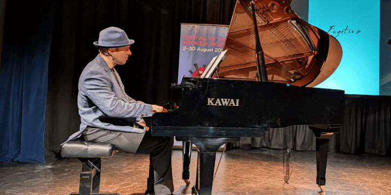 Pianist Simon Tedeschi seated at a black grand piano on stage.