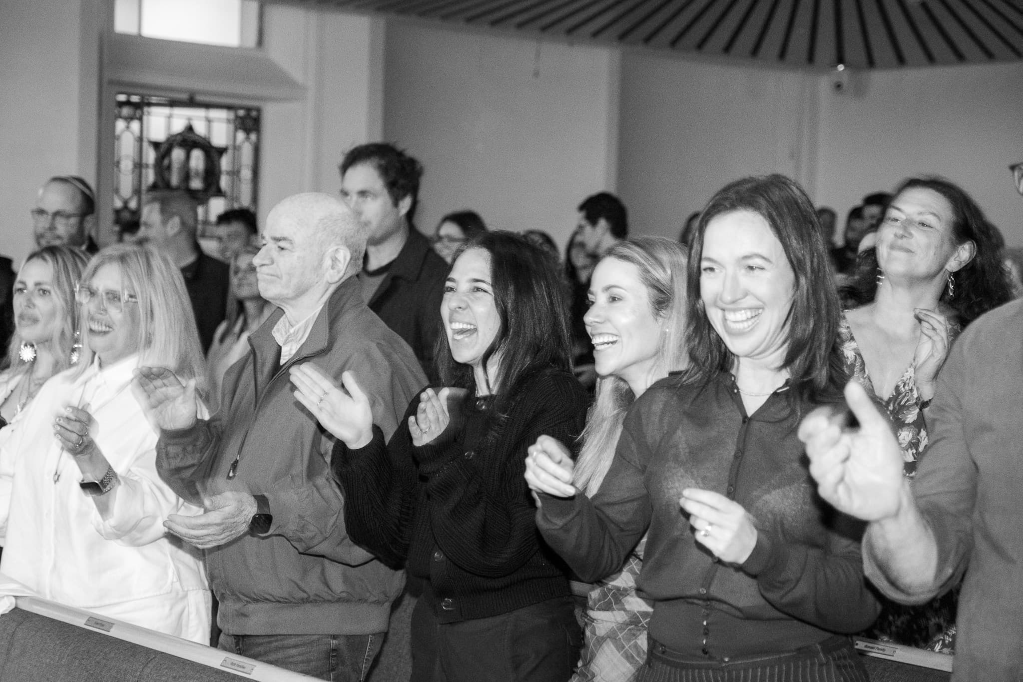 Audience members standing and applauding at You Were Great in Shule, photographed in black and white.