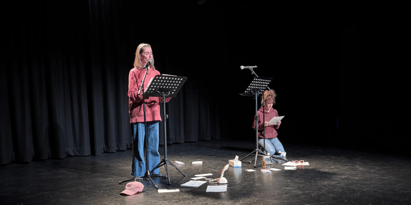 Jessica Chapnik Kahn and Miriam Hechtman reading a new play on stage, with music stands and props arranged on the floor.